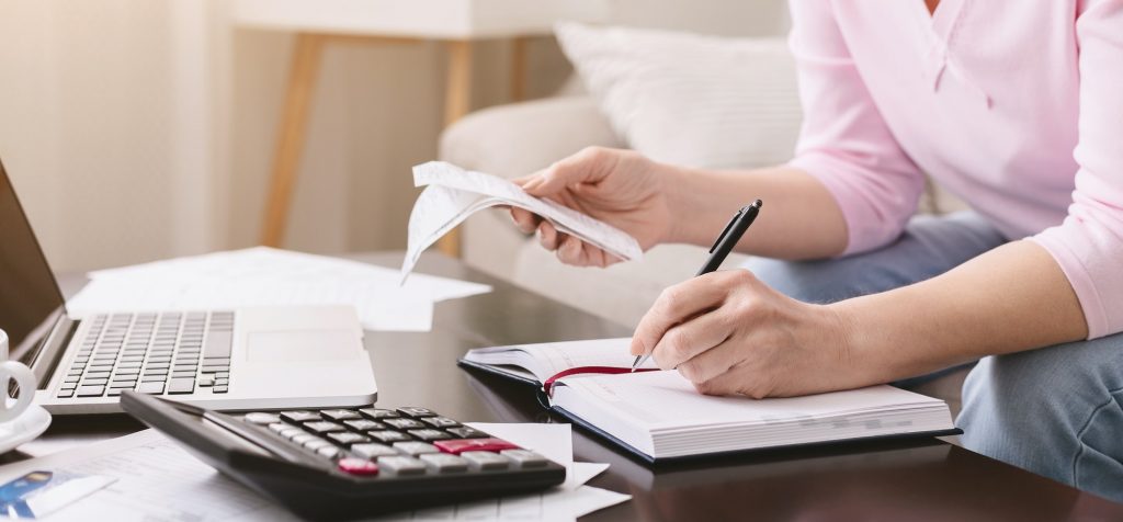 Mature lady with bills noting her purchases at home